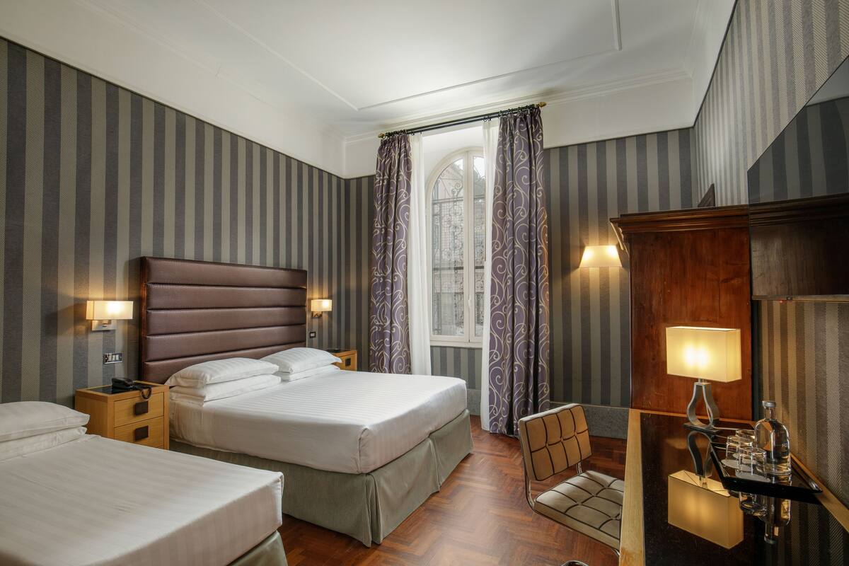 A hotel room with two beds, a sitting area, a mirror, and a window with curtains.