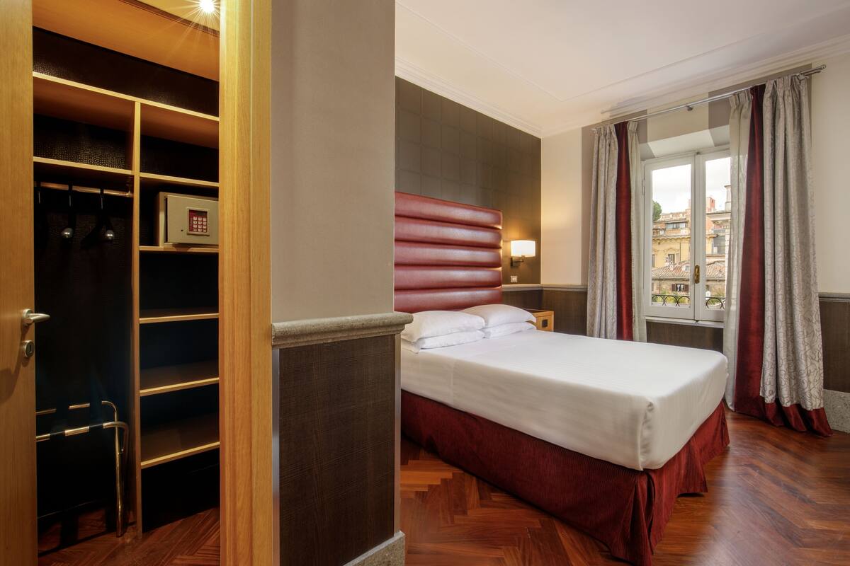 A hotel room with a bed, a wardrobe, a desk, and a window with curtains.