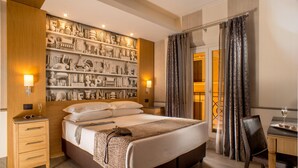 A hotel room with a large bed, wooden headboard, a wall of decorative items, a desk with a chair, and a view through a glass door. - Hotel Royal Court (Rome)