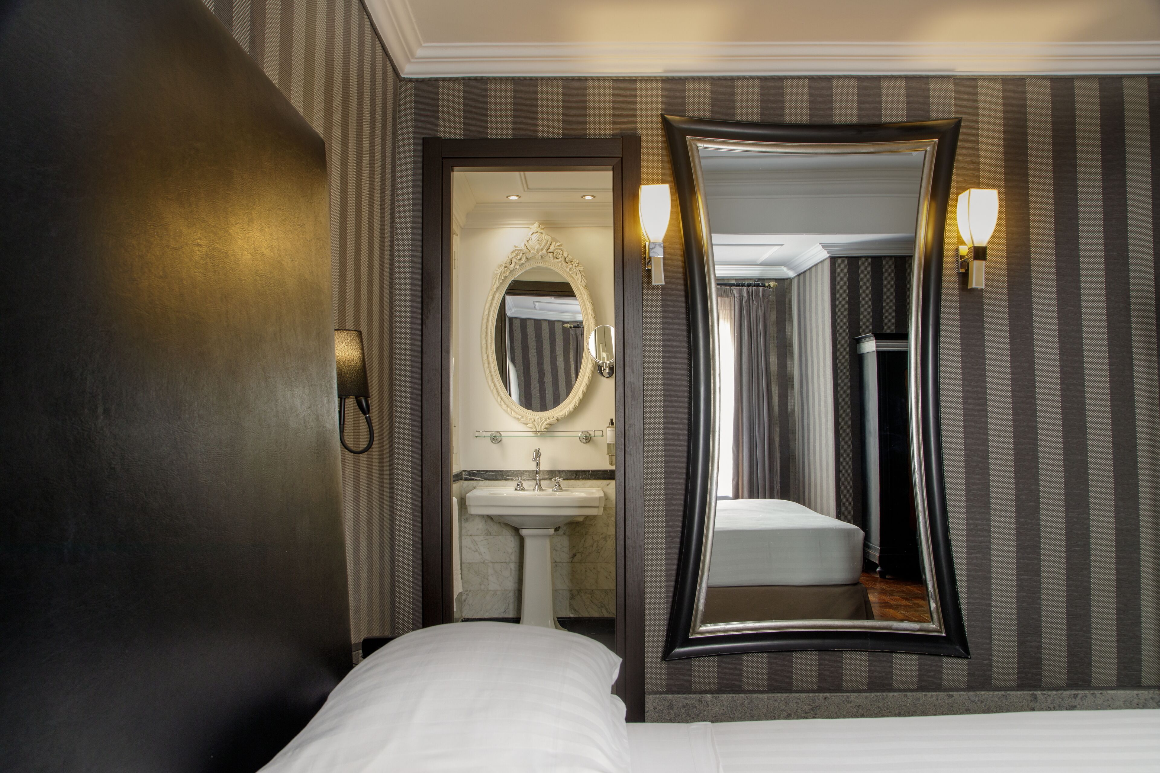 A hotel room with a large bed, a bathroom with a sink and mirror, and a wall-mounted light fixture.