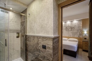 A modern bathroom with a marble wall, a shower, and a bedside table with a lamp.