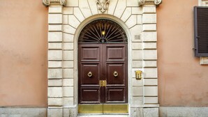 A double wooden door with a metal gate, set within a stone archway, flanked by decorative columns, and a small window to the right. - Hotel Royal Court (Rome)