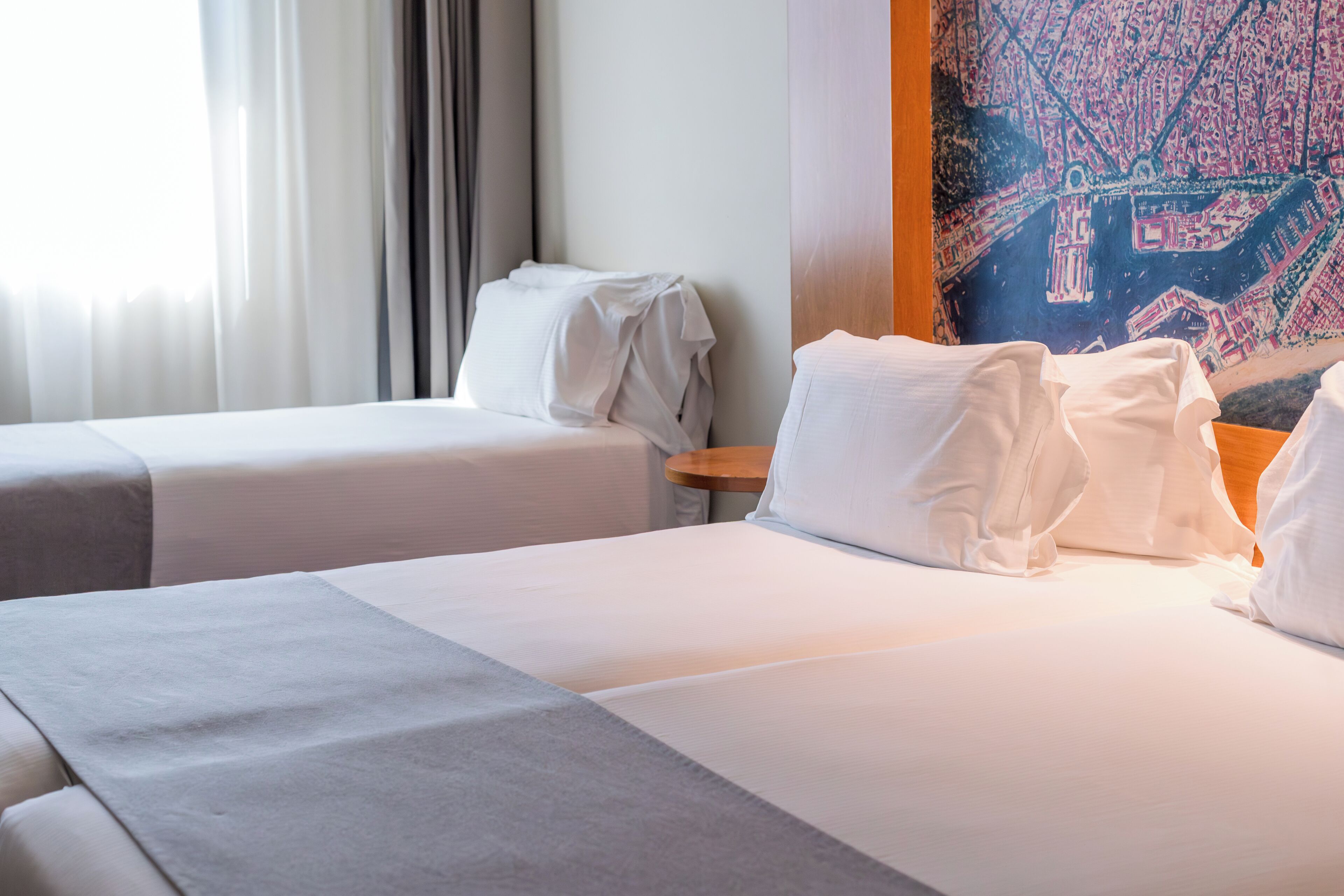 A hotel room with two beds, a wooden headboard, and a large cityscape painting on the wall.