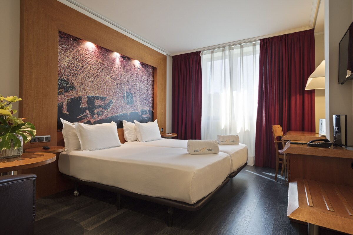 Una habitación de hotel con una cama grande, un escritorio, una silla, un televisor y una obra de arte de gran tamaño en la pared.