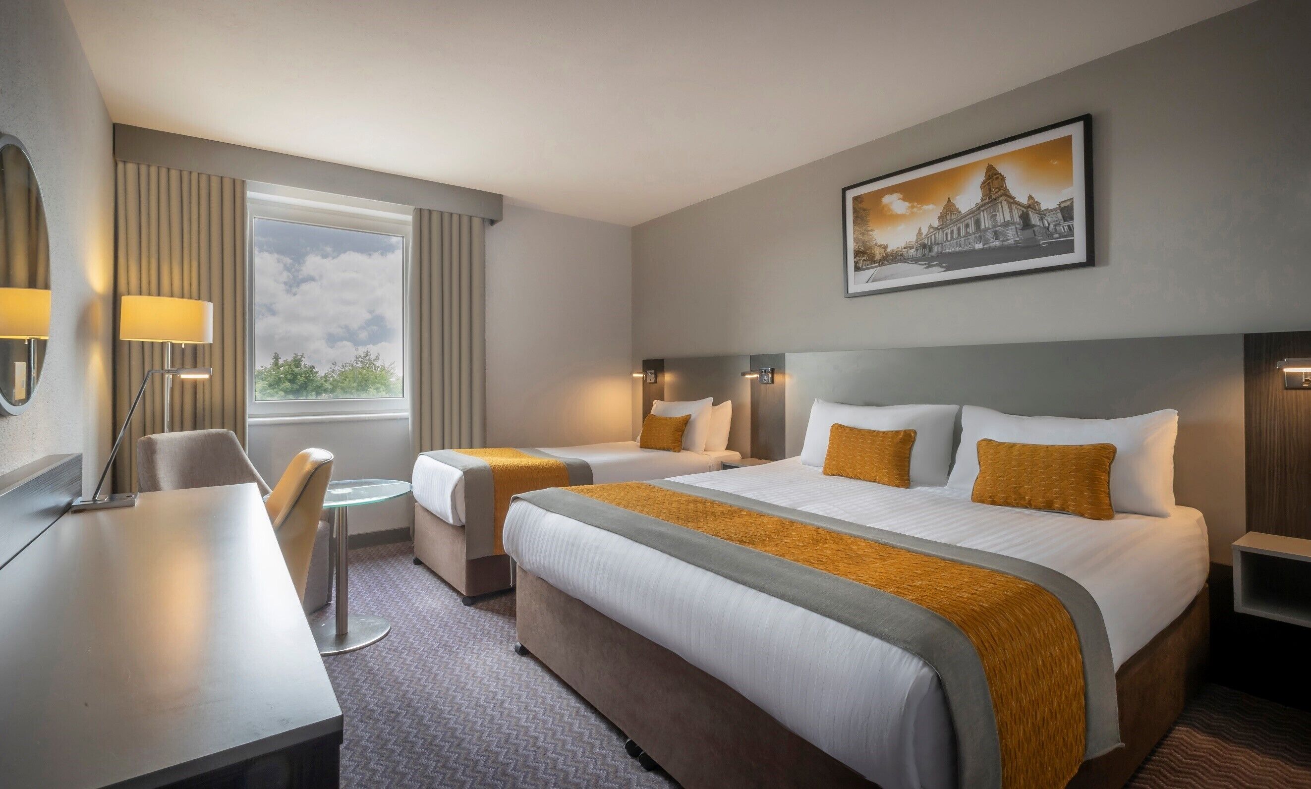A hotel room with two beds, a desk, a chair, a small table, and a window with curtains.