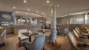Zona moderna de bar con asientos y una barra, que incluye una cafetera y varias botellas.