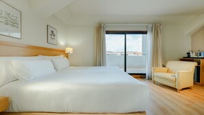 Camera d'albergo con un letto grande, una poltrona, una scrivania e vista sul mare.