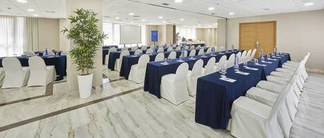 A conference room with multiple tables, white chairs, and a large potted plant.