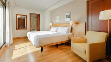 A hotel room with a large bed, a chair, a nightstand, and a wooden floor.