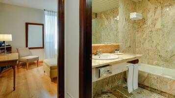 Un baño de hotel moderno con lavamanos de mármol, bañera y ducha.