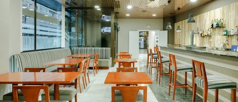 Un restaurante moderno con mesas y sillas de madera, una zona de bar y grandes ventanales con vistas al exterior.