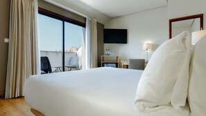 Una camera d'albergo con un letto grande, una scrivania con una sedia, una TV a muro e vista sull'esterno.
