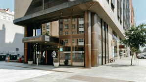 Un edificio moderno con un'ampia entrata, porte in vetro e un cartello con la lettera 'H' ben visibile, che indica un hotel.