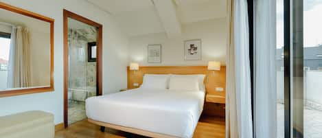 Habitación de hotel con una cama grande, un banco, cabecera de madera y vistas por una puerta de cristal.