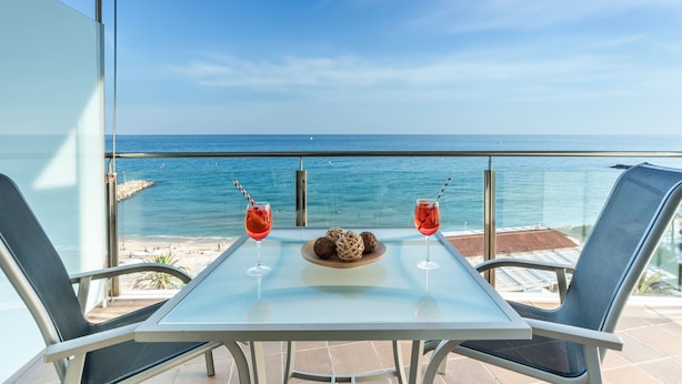 A glass table with two drinks and a plate of snacks on a balcony overlooking the sea. - Hotel Calipolis (Sitges)