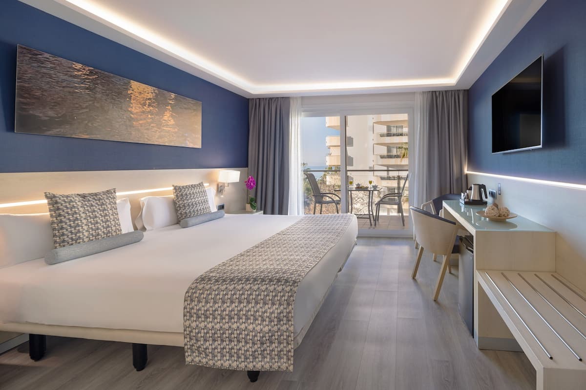 A modern hotel room with a large bed, a desk, and a balcony with a view.