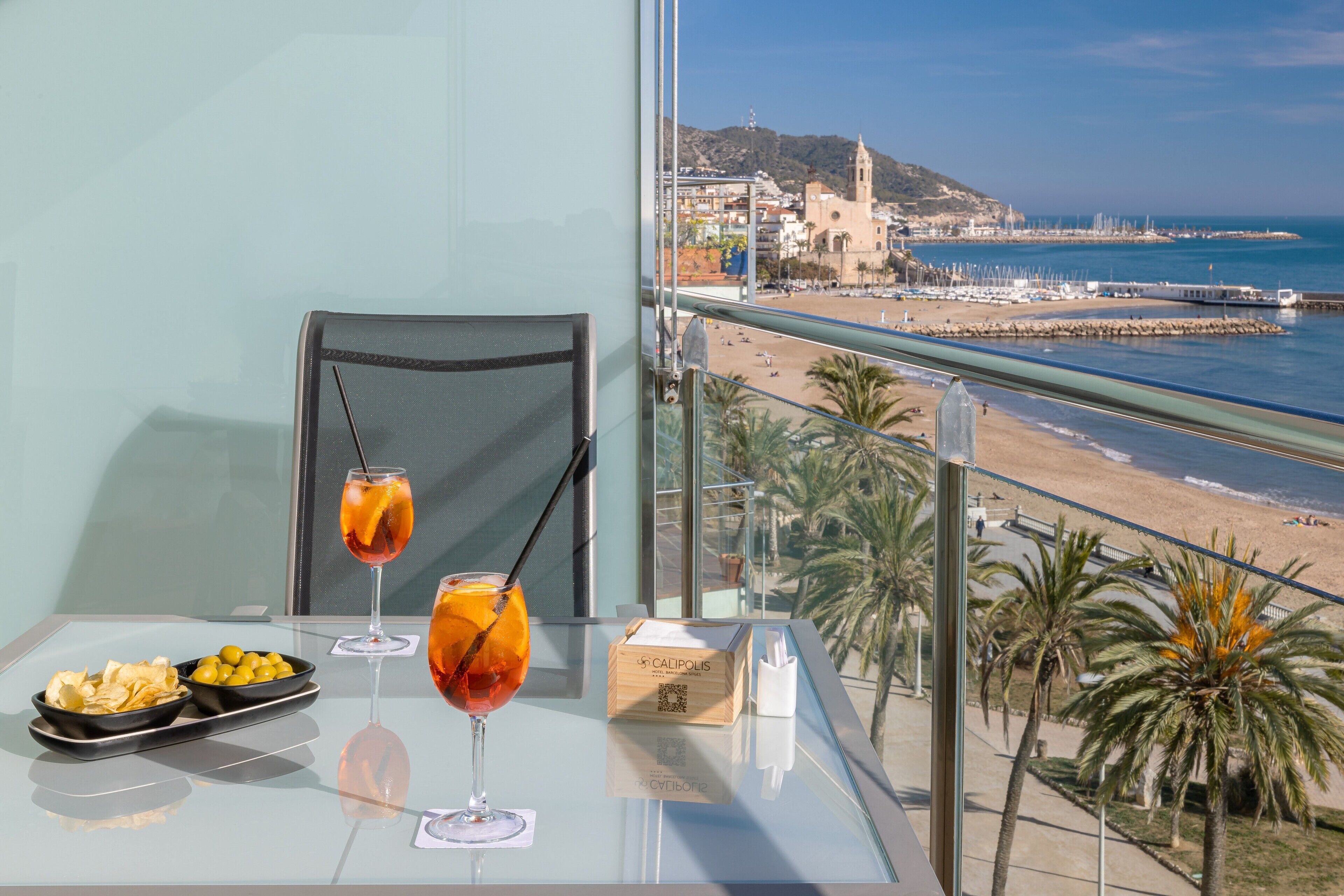Une table avec des boissons et des collations, une chaise, et une vue sur une plage et des bâtiments.