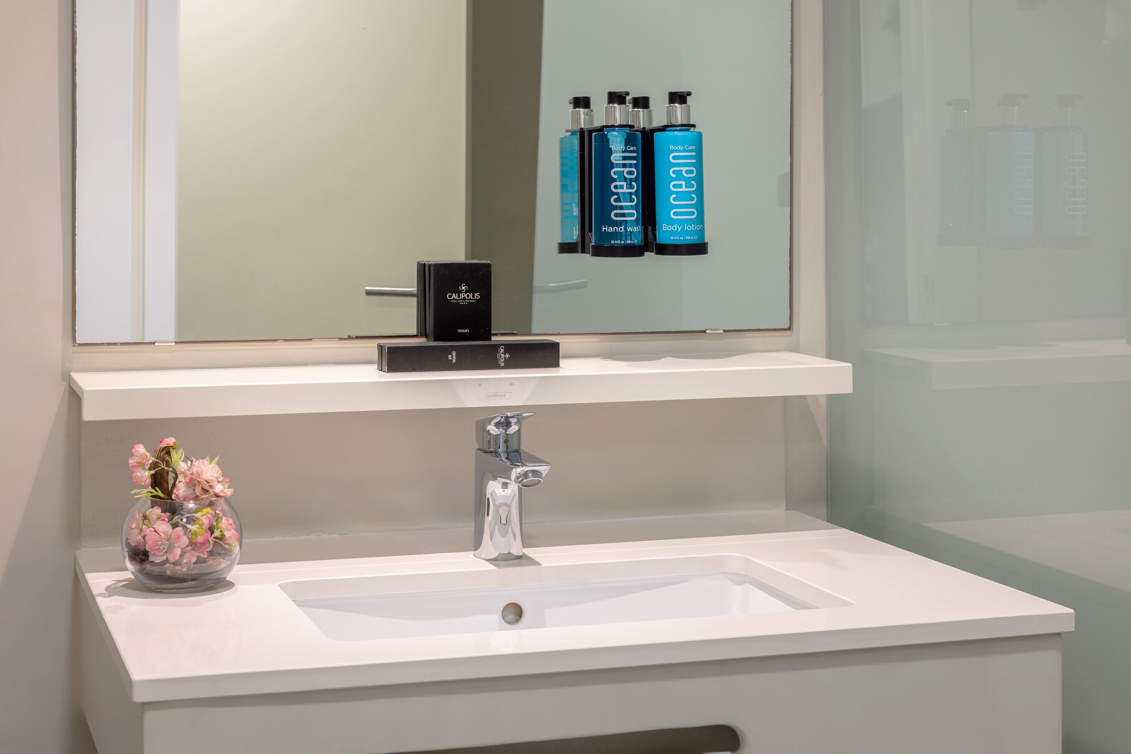 A bathroom with a white sink, a mirror, and a vase of pink flowers.