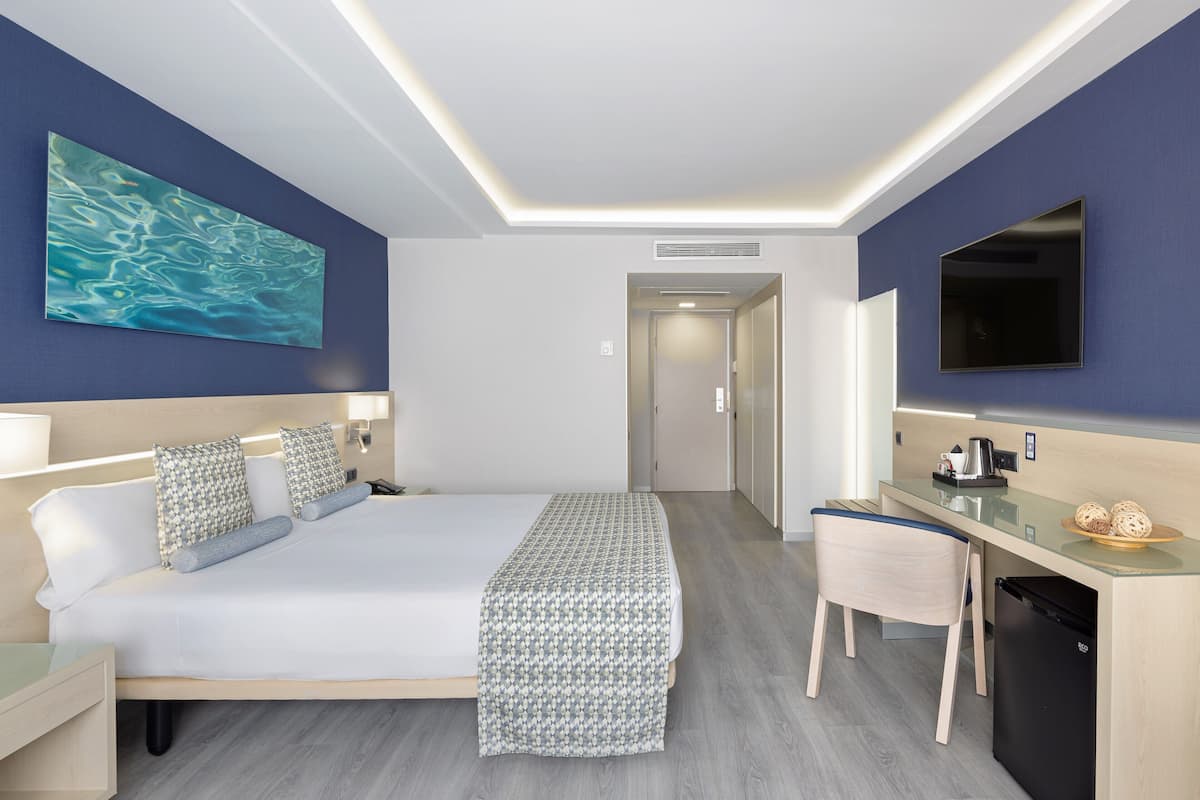 A modern hotel room with a large bed, a desk, a chair, and a TV mounted on the wall.