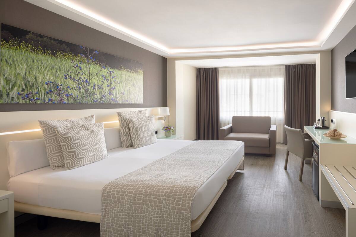A modern hotel room with a large bed, a desk, a chair, and a television.