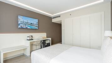 Una habitación de hotel moderna con una cama grande, un escritorio con cafetera, un televisor montado en la pared y un armario.