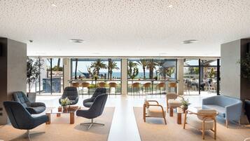 Eine großzügige Lobby mit moderner Sitzgelegenheiten, großen Fenstern und Blick auf Palmen.