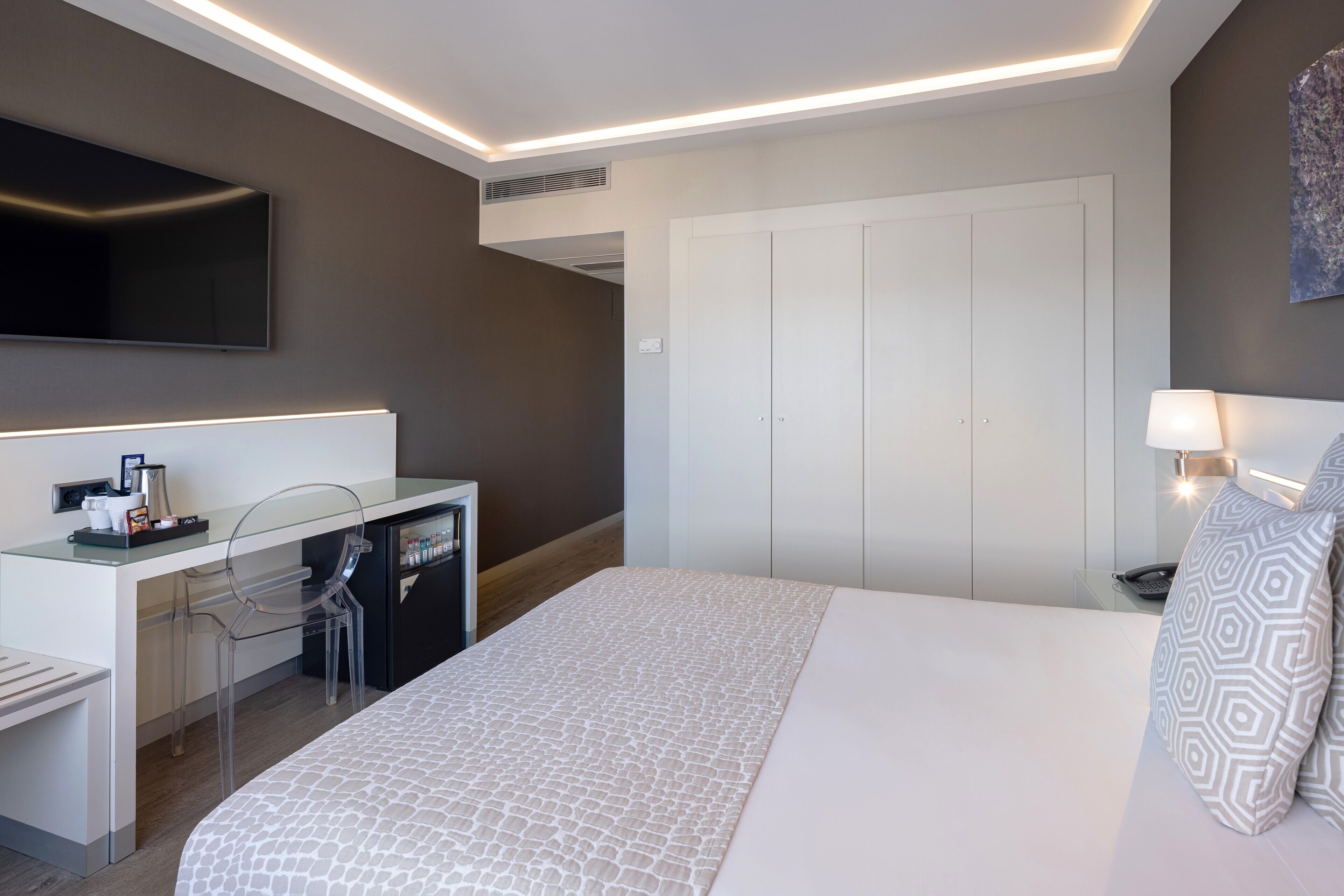 Una habitación de hotel moderna con una cama, un escritorio con una silla, un televisor y un armario.