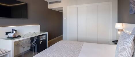 Una habitación de hotel moderna con una cama, un escritorio con una silla, un televisor y un armario.