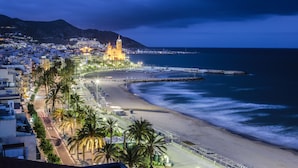 A coastal cityscape with a prominent church, a beach, and a promenade lined with palm trees. - Hotel Calipolis (Sitges)