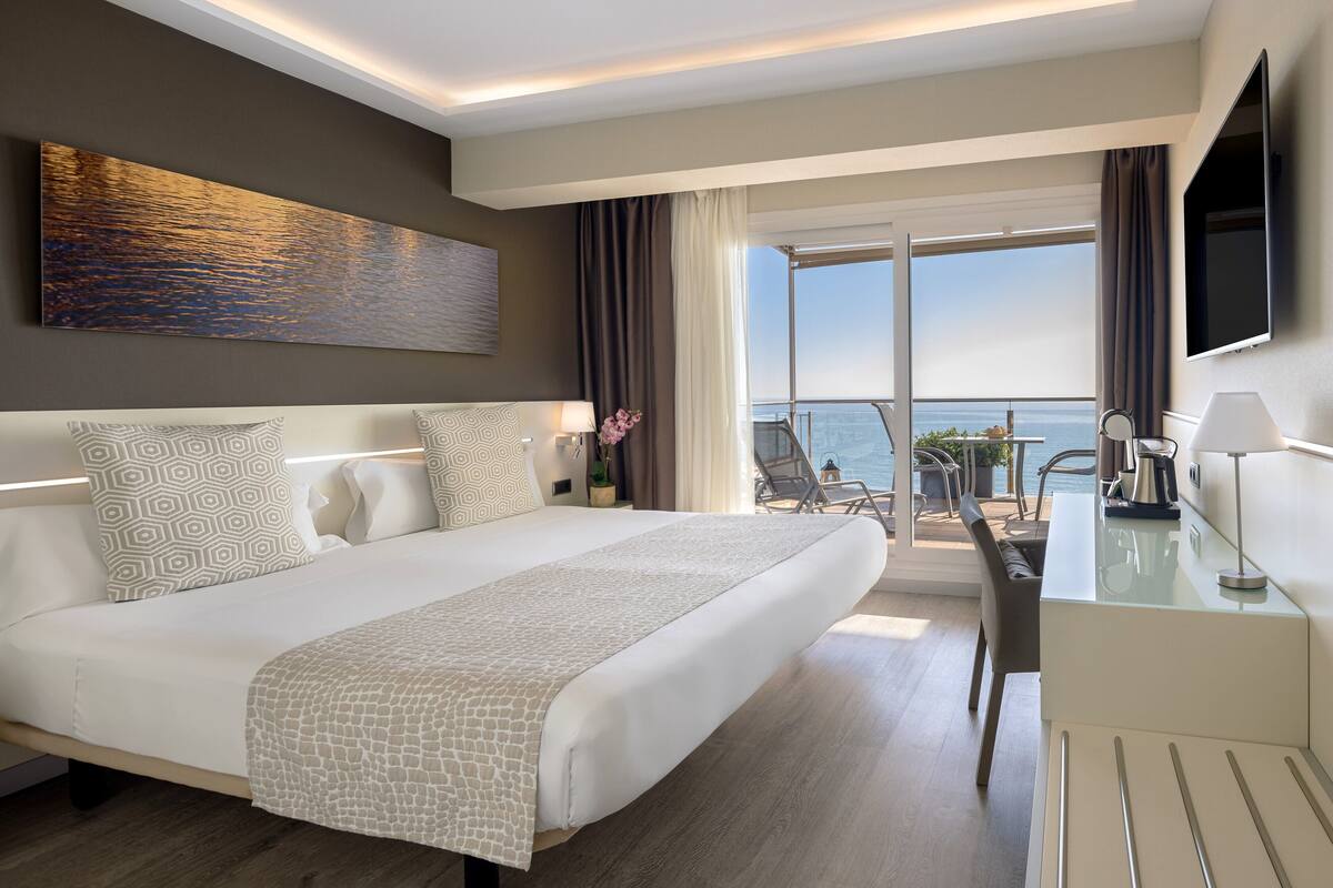 A modern hotel room with a large bed, a desk, and a view of the ocean.