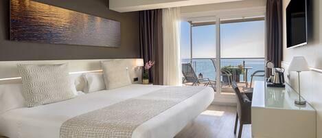 A modern hotel room with a large bed, a desk, and a view of the ocean.