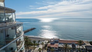 A coastal hotel with a balcony overlooking the sea, a rocky breakwater, and a palm-lined promenade. - Hotel Calipolis (Sitges)