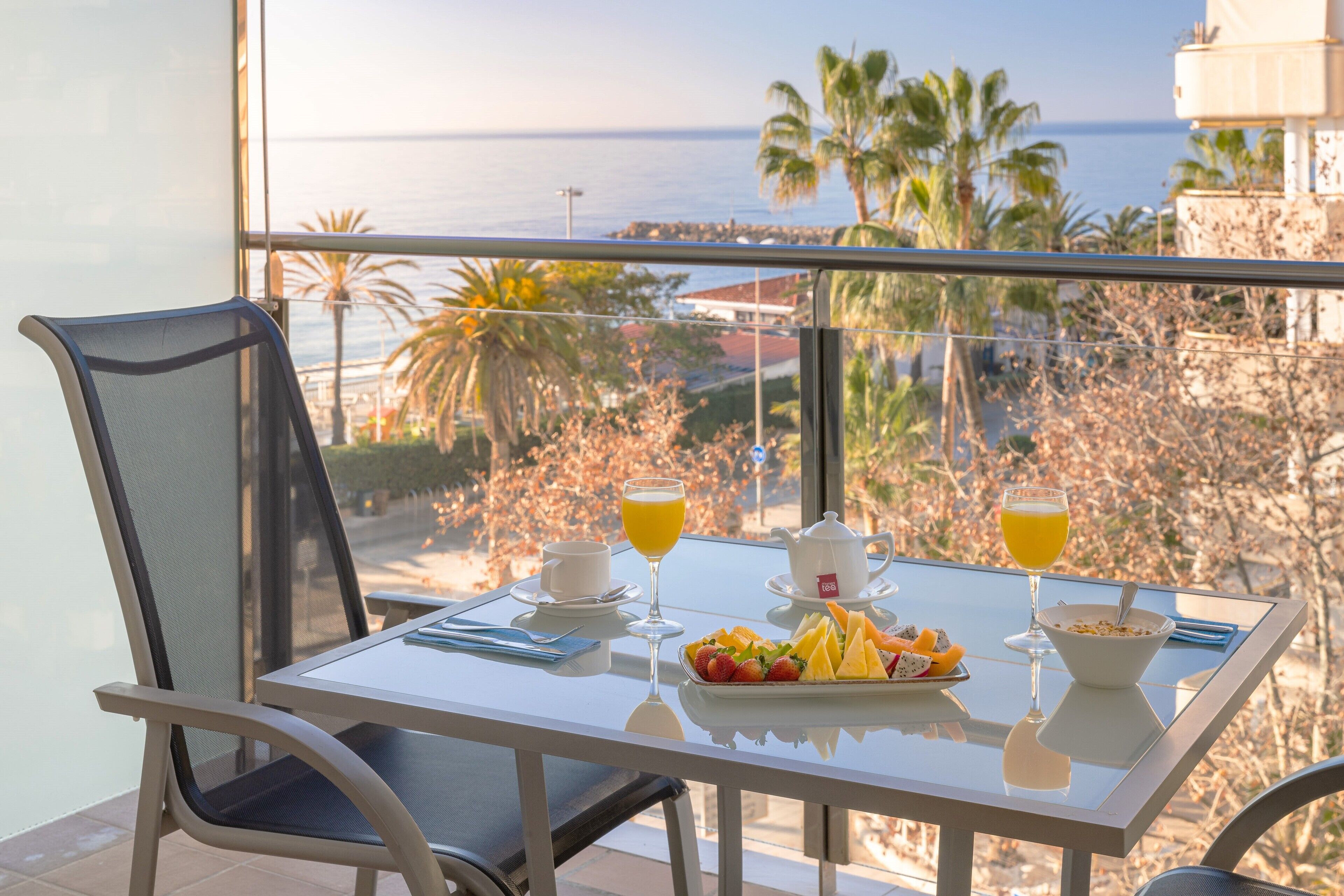 A dining table with breakfast items and a glass of orange juice, overlooking a scenic view of the ocean and palm trees.