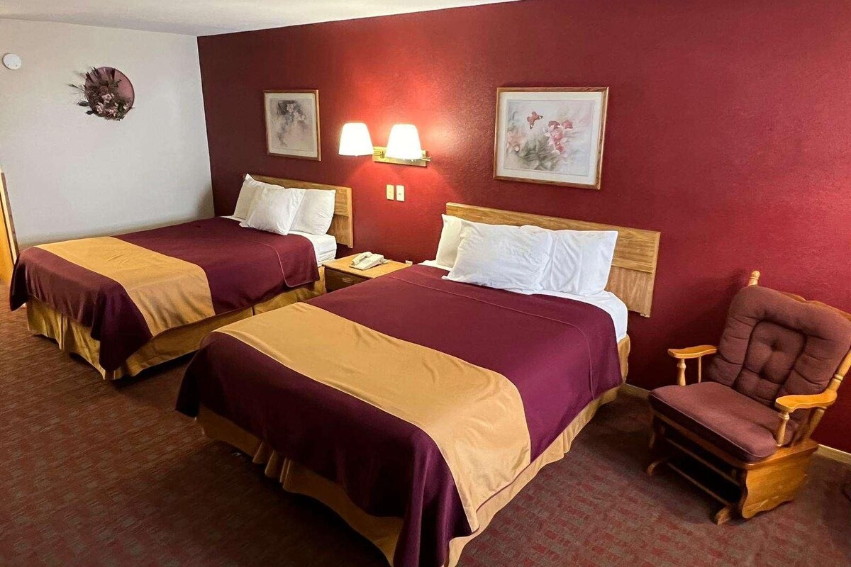 A hotel room with two beds, a wooden chair, and a small table.