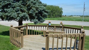 A wooden deck with a lattice railing, a tree, and a flower pot. - Americas Best Value Inn Suburban Motel (Emmetsburg)