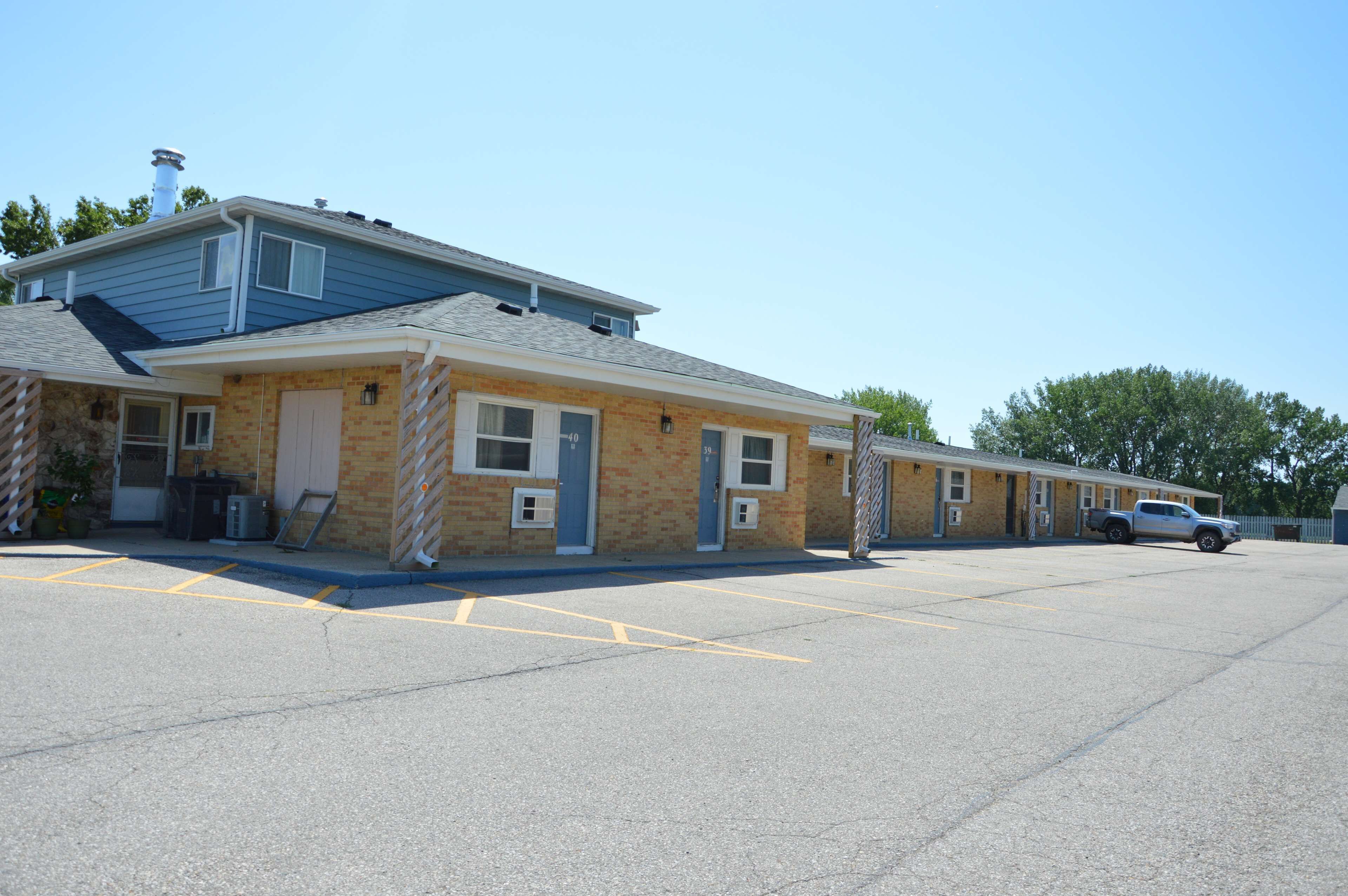 A motel with a row of rooms, a parking lot, and a single-story building with a blue roof.