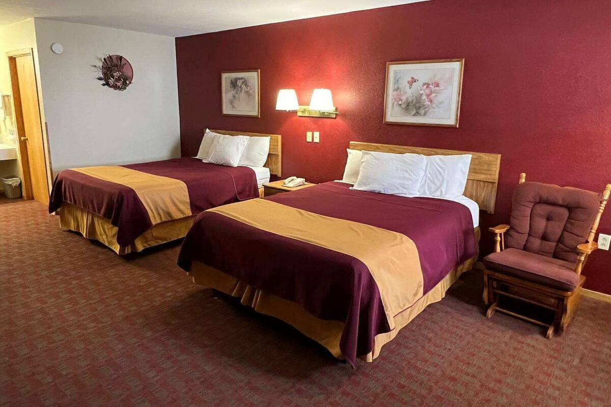 A hotel room with two beds, a chair, and a nightstand with a lamp.