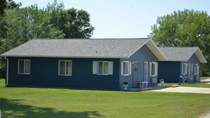 A two-story blue house with a sloped roof, white shutters, and a small porch with a flag. - Americas Best Value Inn Suburban Motel (Emmetsburg)