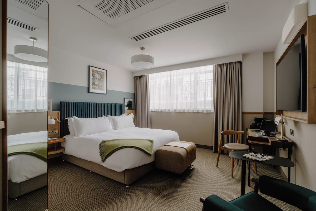 A hotel room with a large bed, a desk with a computer, a chair, and a small table.