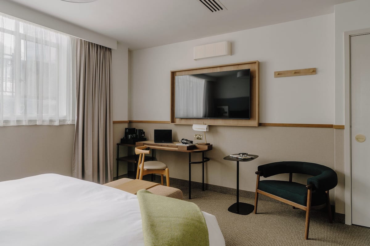A hotel room with a bed, a desk with a computer, a chair, a small table, and a mirror on the wall.