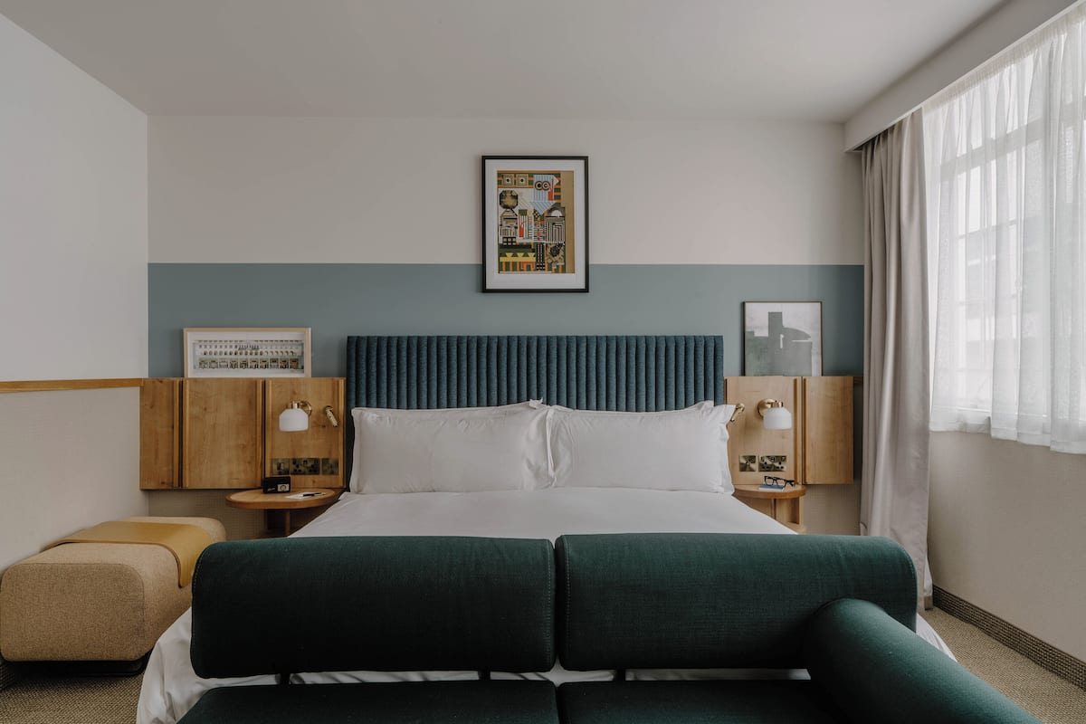 A hotel room with a bed, two bedside tables, a wall-mounted picture, and a window with curtains.