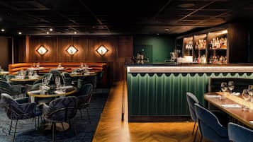 Uma área de bar com balcão verde, diversos arranjos de assentos e variedade de garrafas.