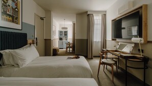 A hotel room with two beds, a desk with a chair, a television, and a kitchenette in the background. - Club Quarters Hotel London City, London (London)
