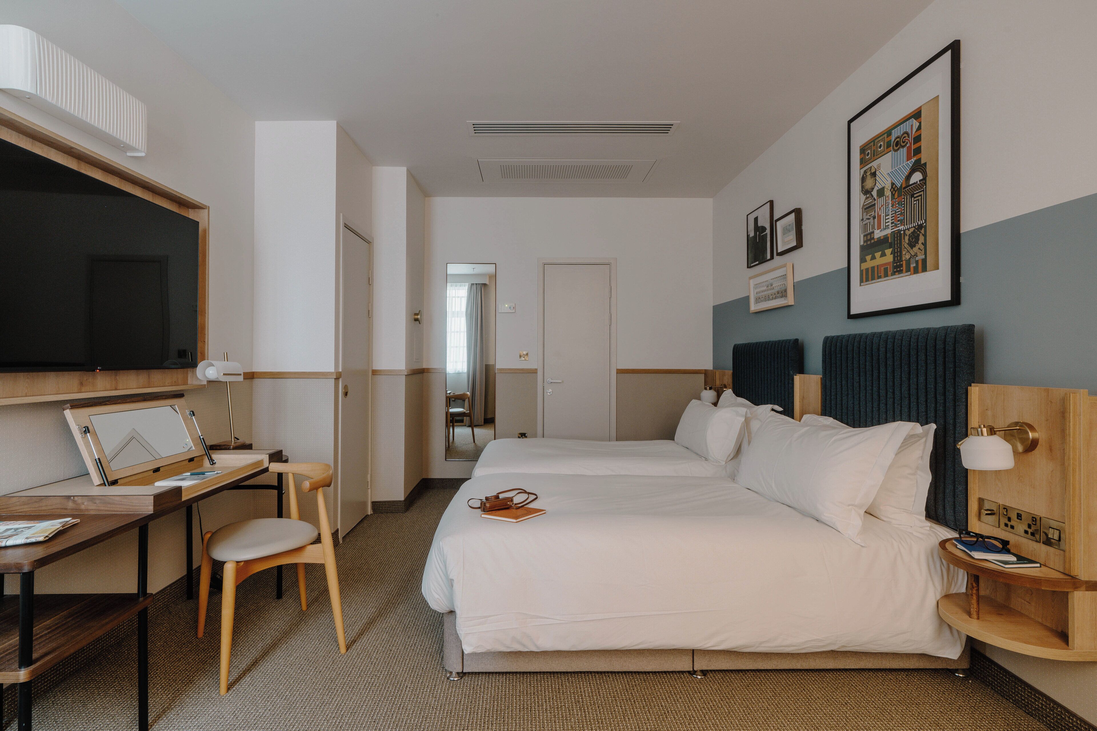 A hotel room with a bed, desk, chair, and a TV.