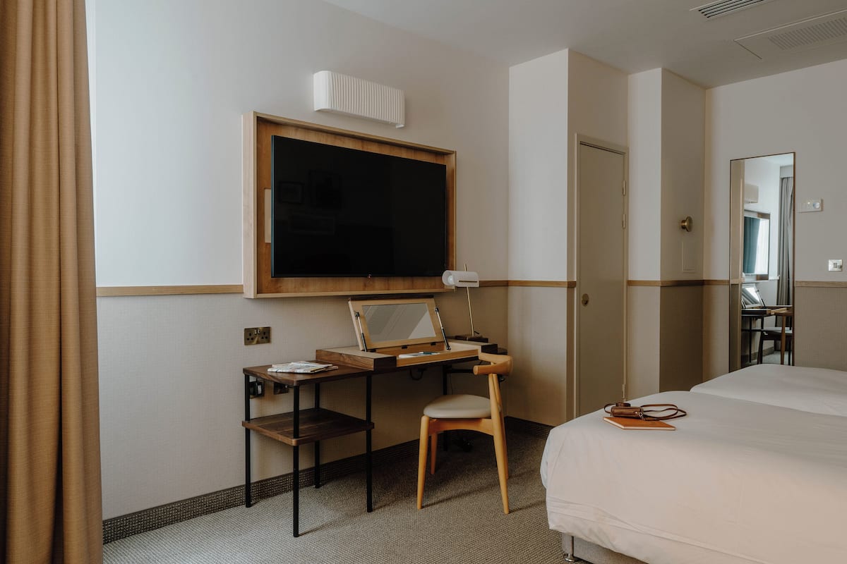 A hotel room with a bed, a desk with a chair, a large mirror, and a window with curtains.