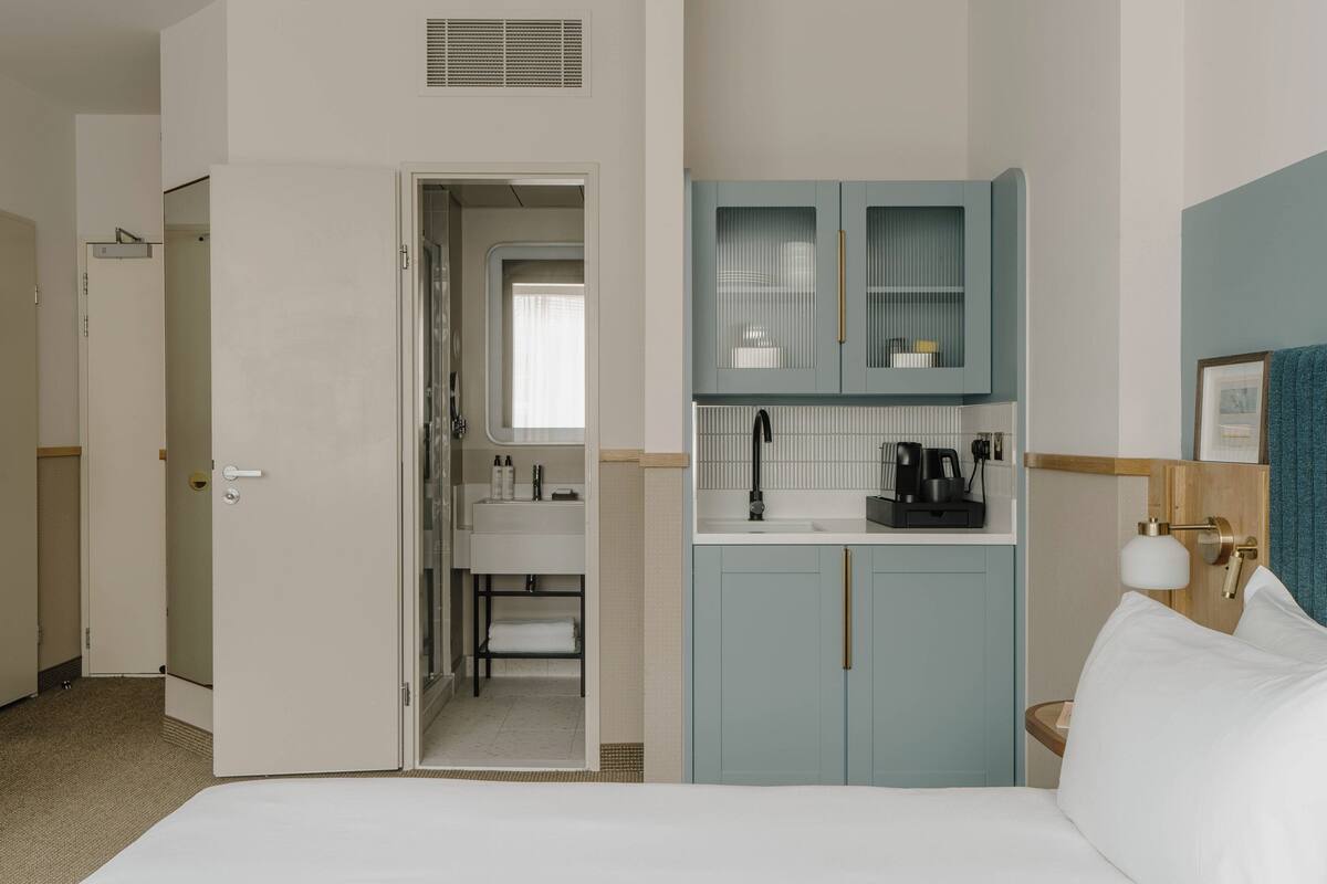 A hotel room with a bed, a bathroom with a sink and mirror, and a kitchenette with cabinets and a coffee maker.