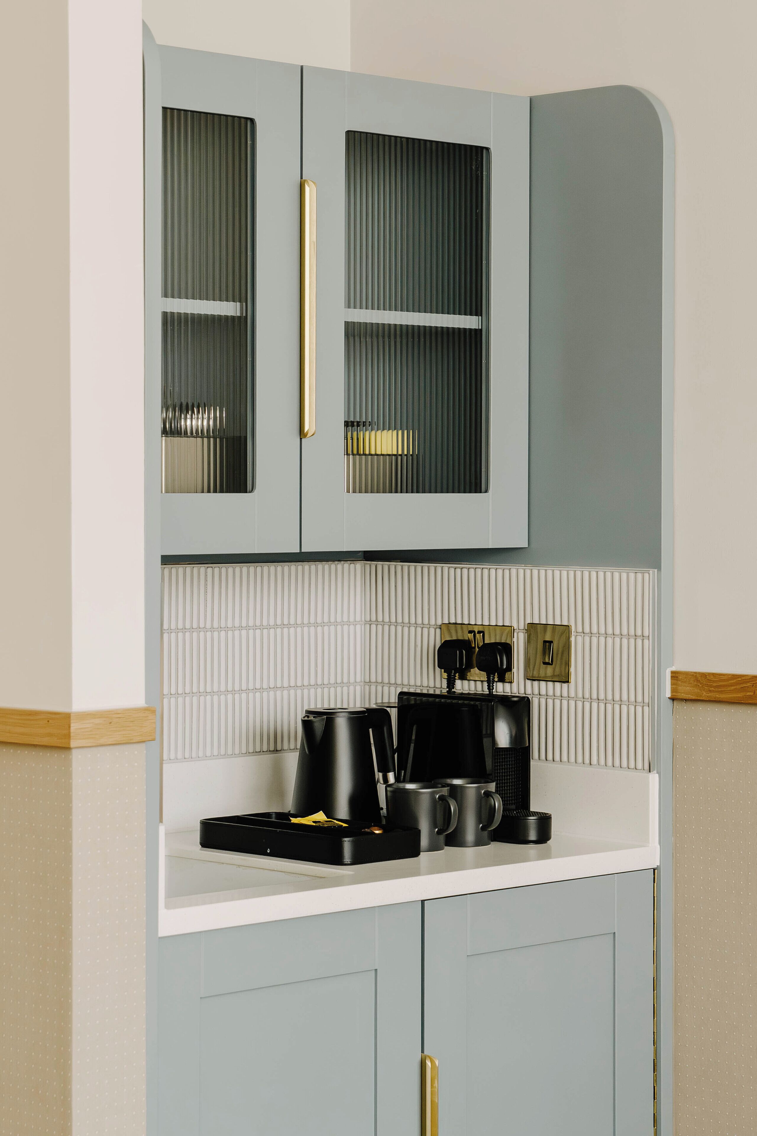 A kitchen with light blue cabinets, a white countertop, and a coffee machine.