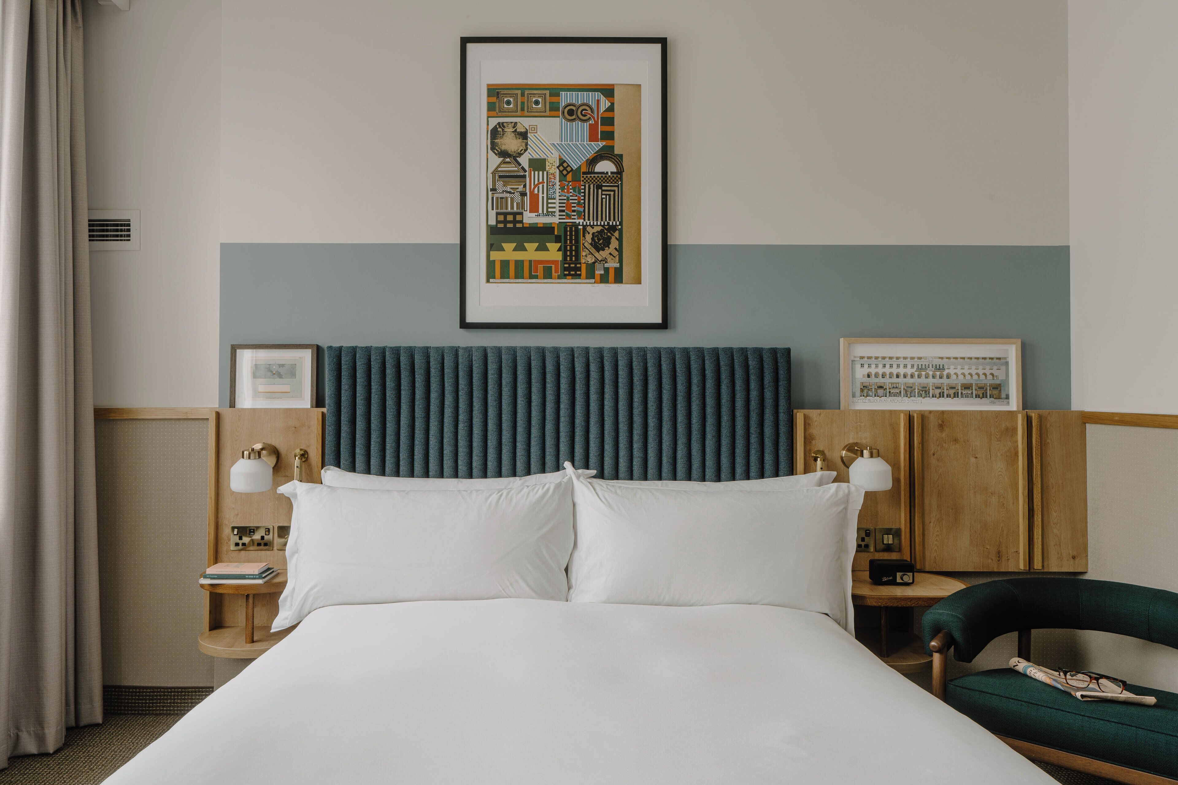 A hotel room with a large bed, a headboard, a framed picture on the wall, a nightstand with a lamp, and a chair.