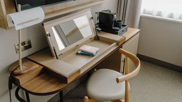 Un bureau en bois avec un écran d’ordinateur, une lampe, un clavier, une machine à café et une chaise.