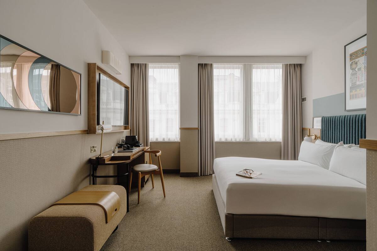 A hotel room with a bed, desk, chair, and a large mirror.